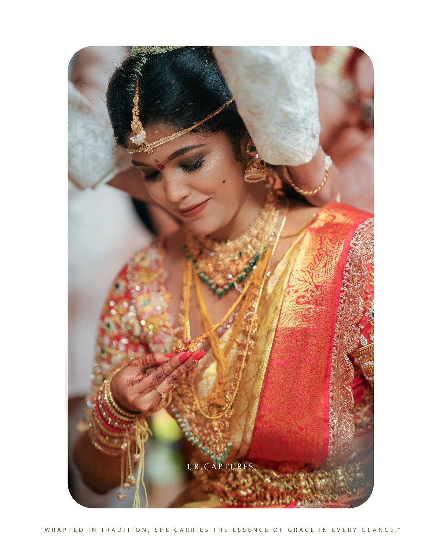 A bride in a red and gold saree adjusting her wedding jewelry